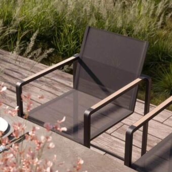 Alura armchair, dark gray metal frame, woven mesh seat, copper armrests, rectangular silhouette, minimalist legs, outdoor deck setting.