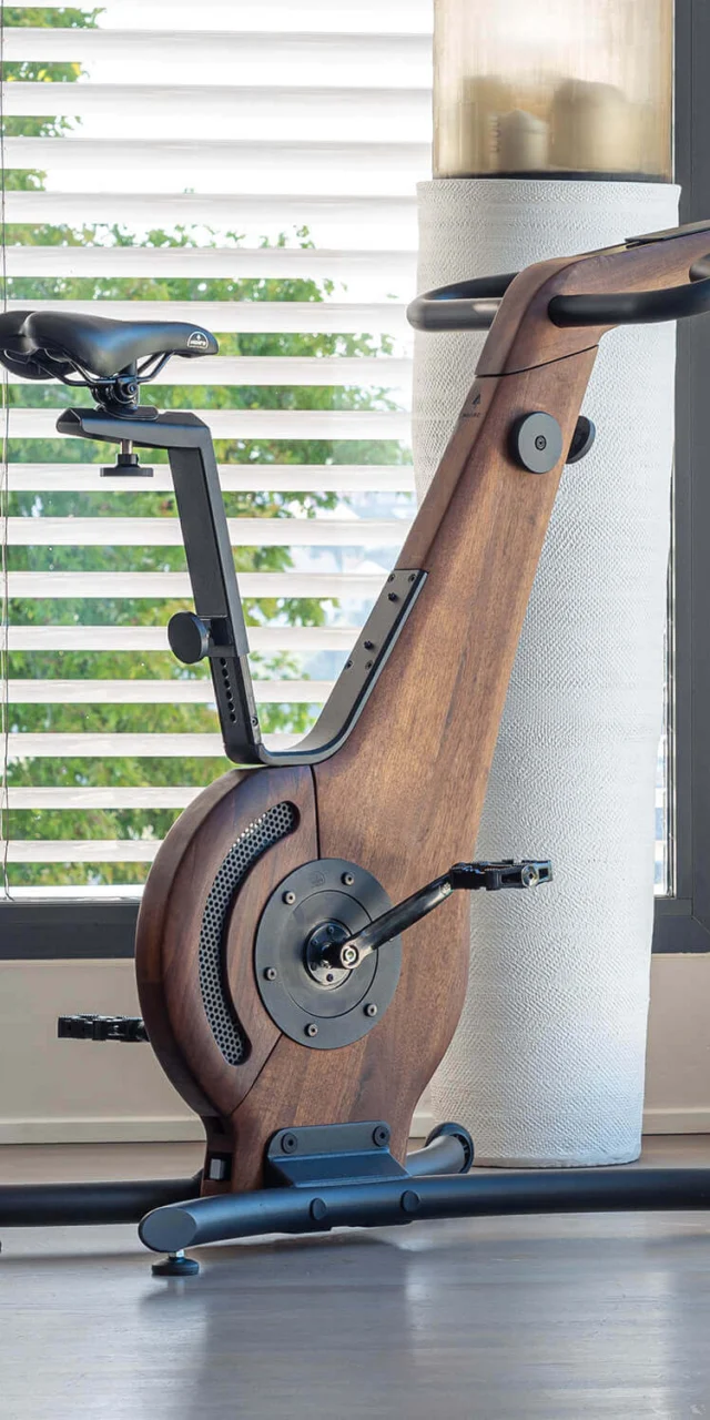 Waterrower NohrD exercise bike with dark walnut wood frame, curved design, black handlebars, and adjustable saddle in a modern interior.