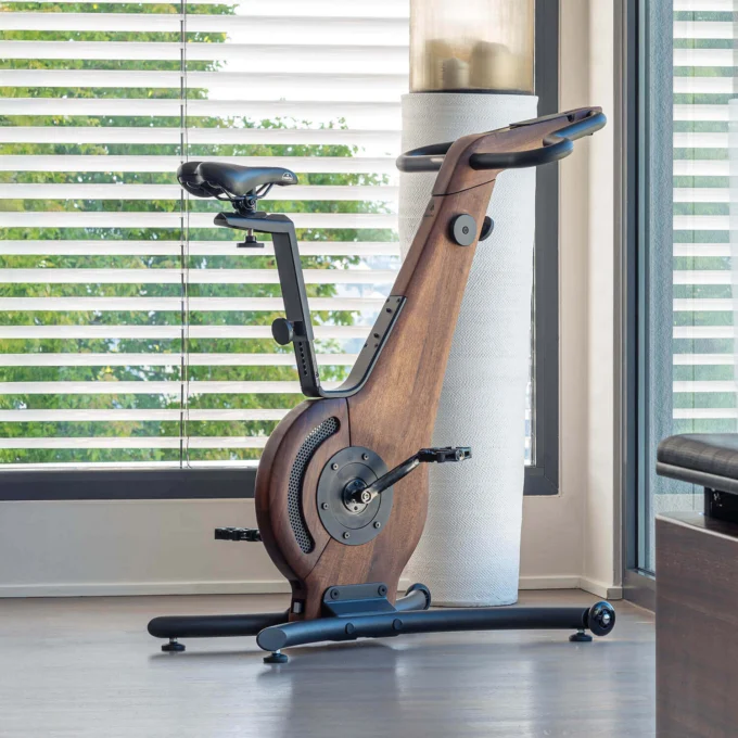 Waterrower NohrD exercise bike with dark walnut wood frame, curved design, black handlebars, and adjustable saddle in a modern interior.