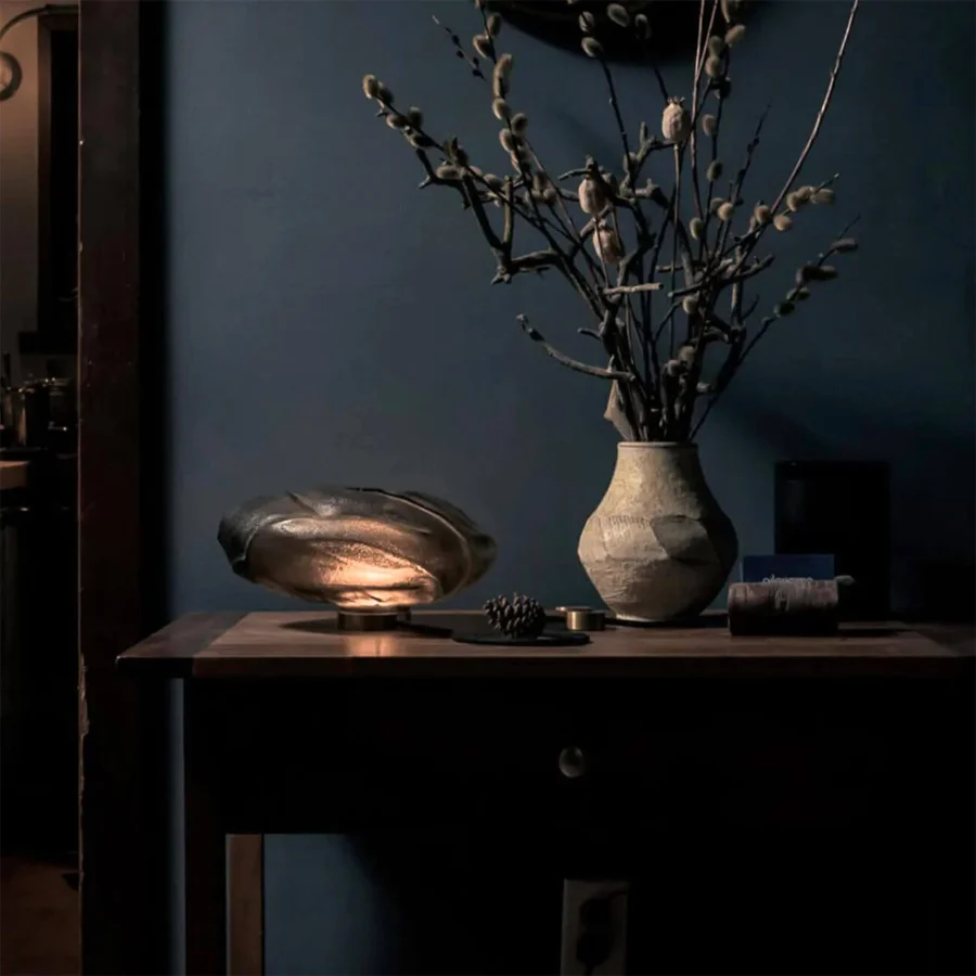 Table lamp by Bocci with glass diffuser and dark gray metal base, showing an organic horizontal silhouette plus amber glow